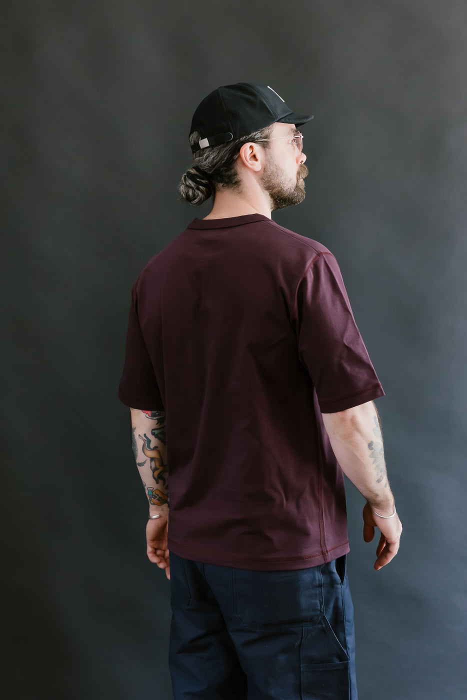 Man wearing a maroon t-shirt and black cap against a dark background