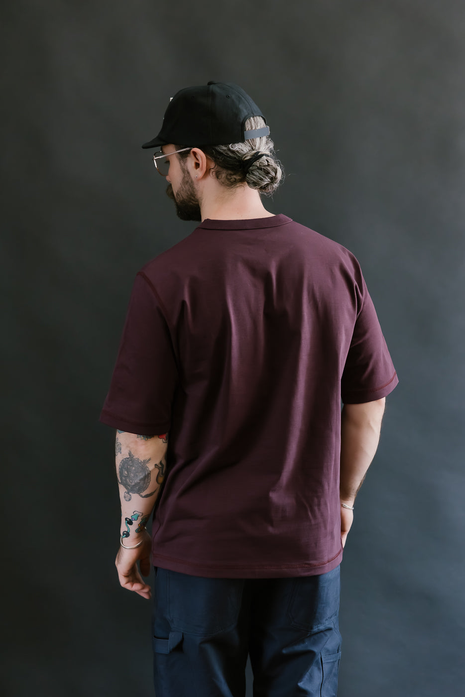 Man wearing a maroon t-shirt and black cap from behind on a dark background
