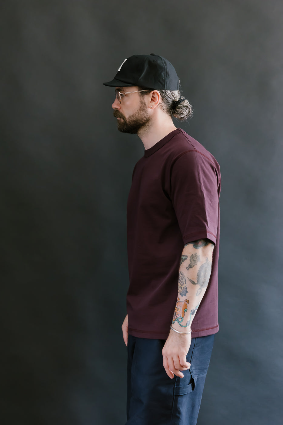 Man wearing a maroon t-shirt and black cap against a dark background