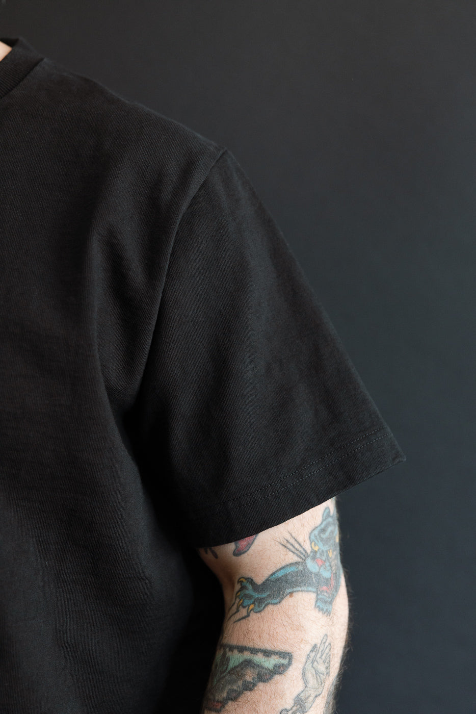 Close-up of male model’s left side showing black tee sleeve hem and shoulder seam, athletic build