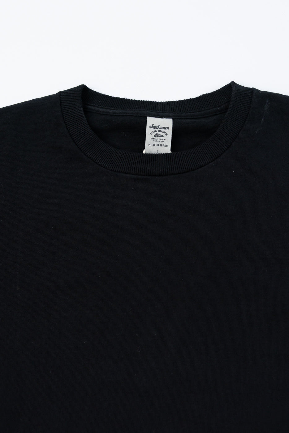 Black crewneck sweater close-up showing front collar, ribbed neckline, and Jackman brand tag with 'Made in Japan' detail.