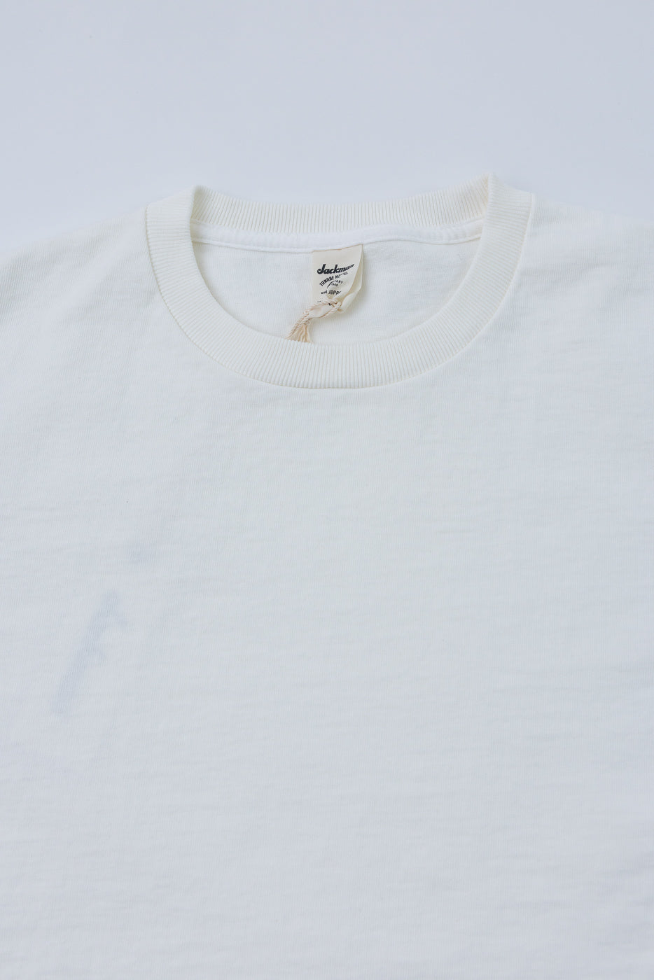 Close-up front view of cream crewneck tee, ribbed collar, Jackman tag visible, soft cotton texture