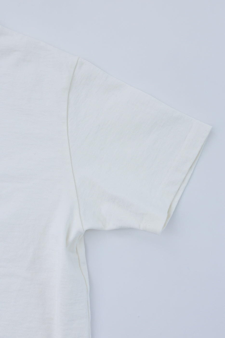 Close-up of off-white tee shirt sleeve and shoulder seam, showing fabric texture and hem detail