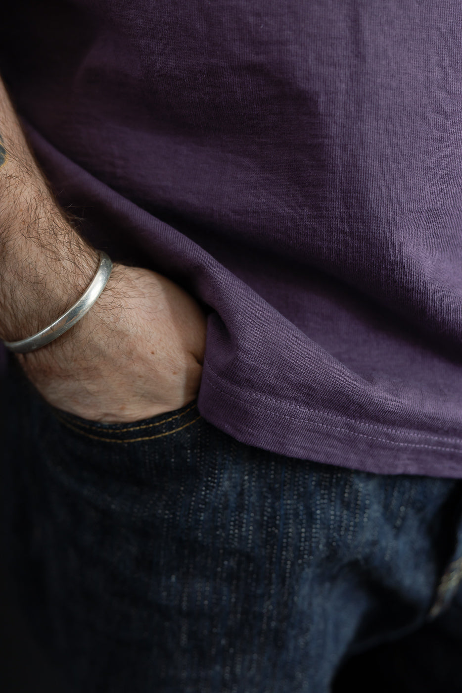 Close-up of male model's side, showing purple tee hem and dark denim texture, hand in pocket, 5'9