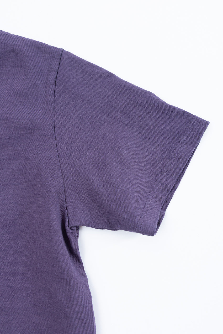 Close-up front view of purple t-shirt sleeve and shoulder seam, showing fabric texture and clean stitching.