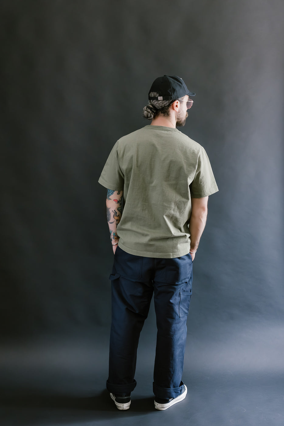 Person wearing a green t-shirt and dark pants against a gray background