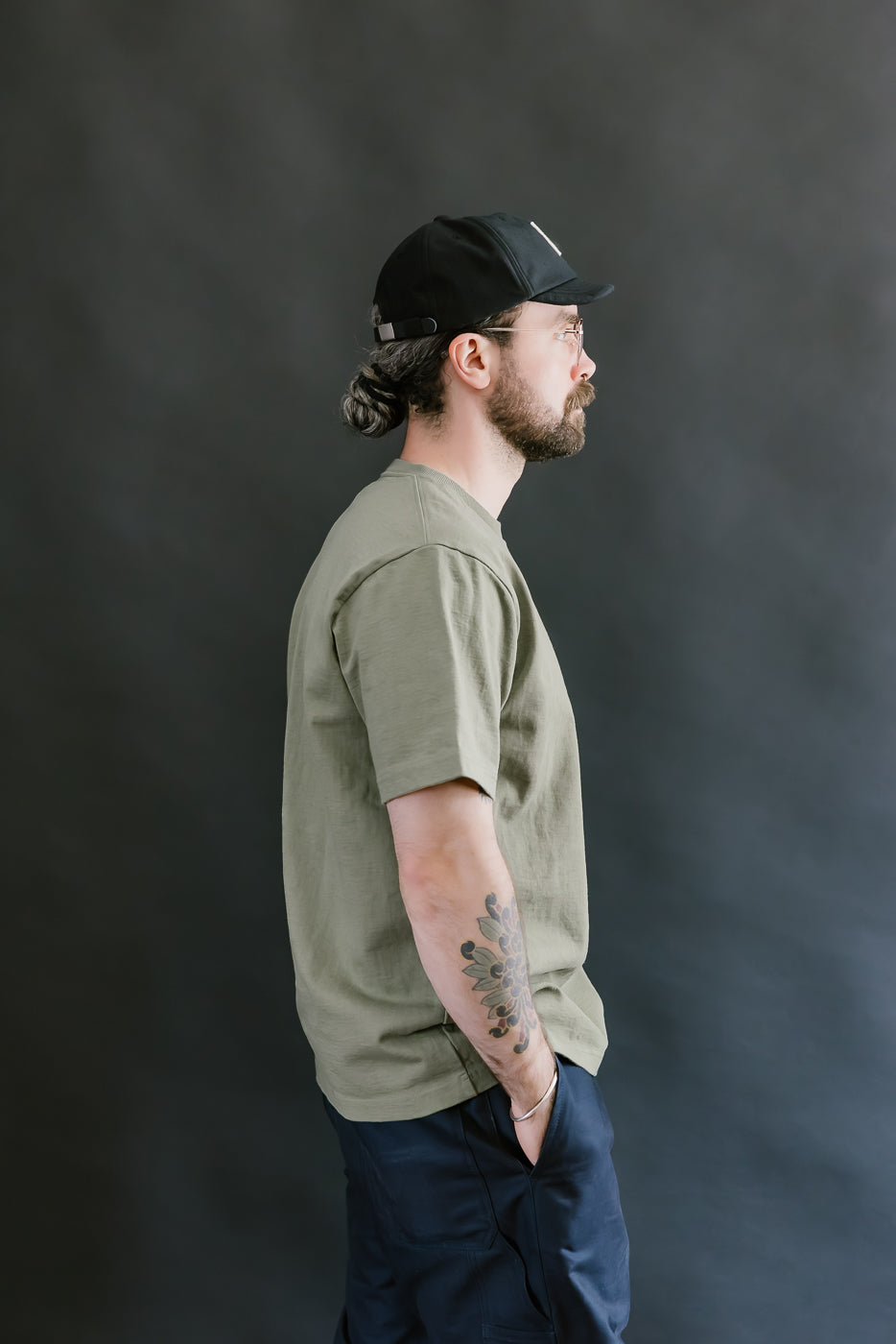 Man wearing a green t-shirt and black cap against a dark background