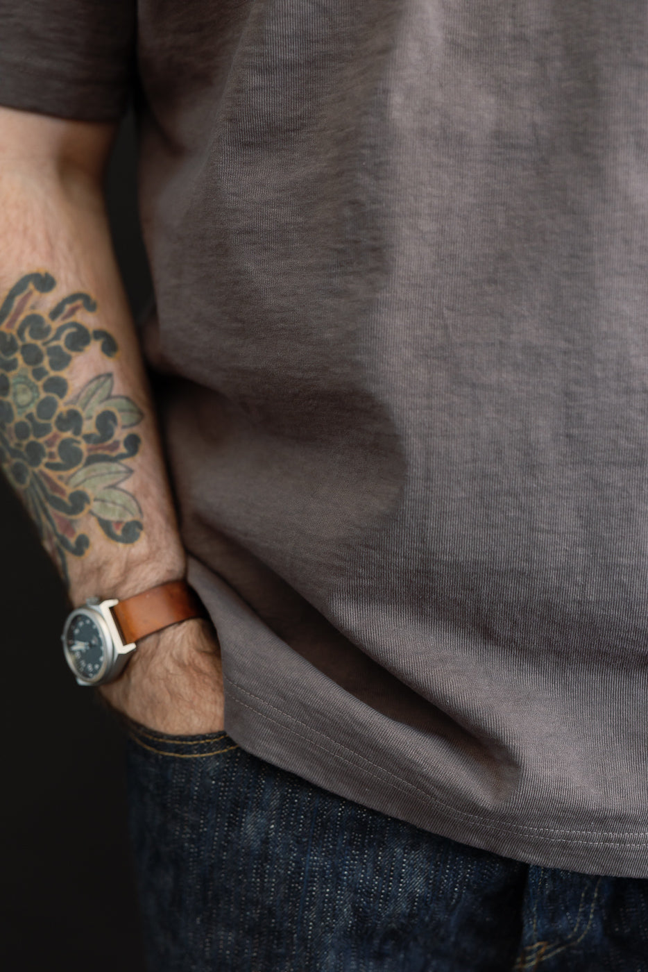Close-up of male model's side, showcasing gray tee hem and denim texture, athletic build, tattooed arm