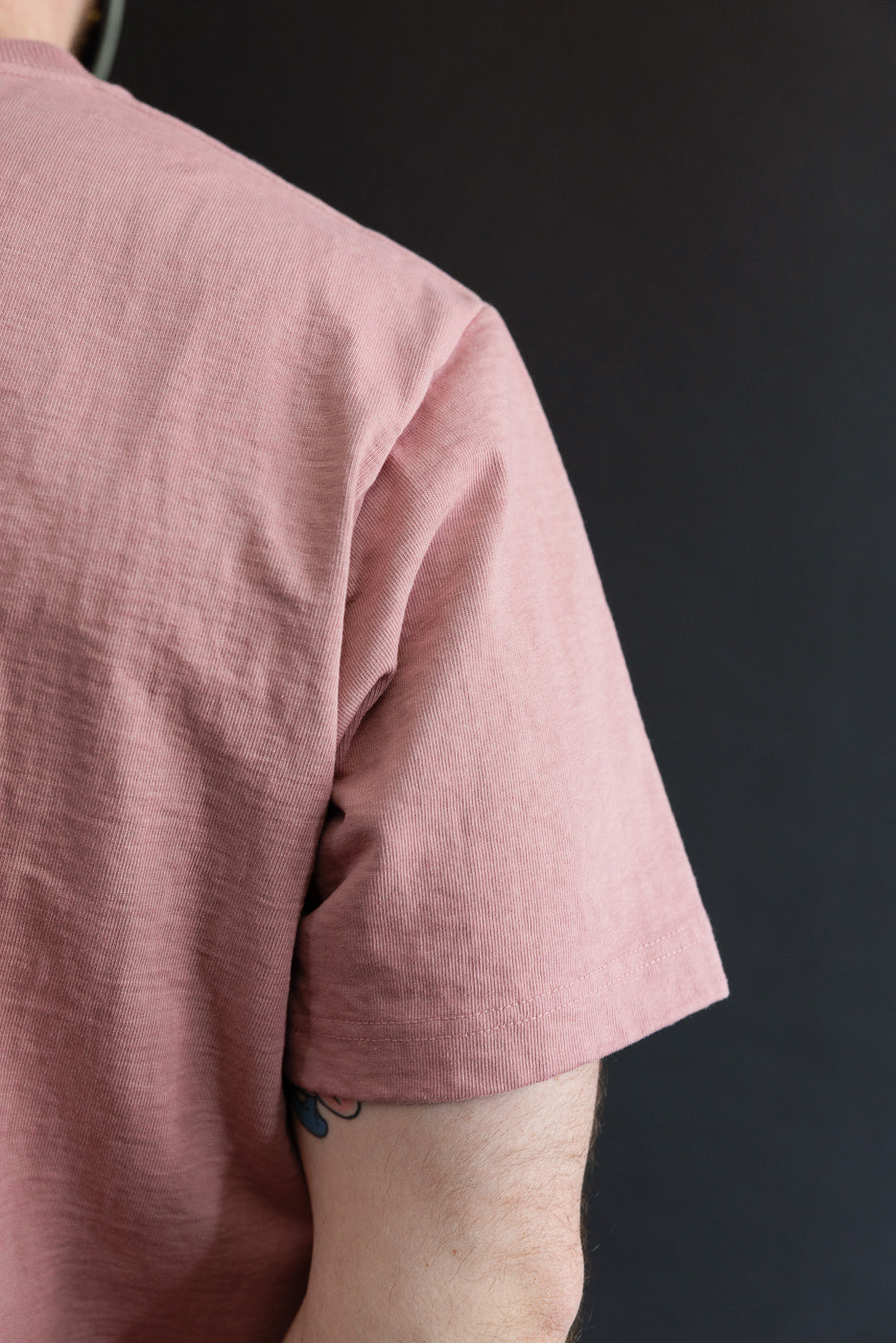 Close-up of male model's left shoulder and sleeve, showcasing pink ribbed T-shirt texture and hem detail.