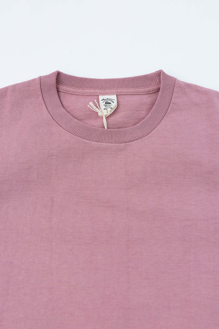 Close-up front view of dusty pink crewneck sweater, showcasing ribbed collar and brand tag detail.