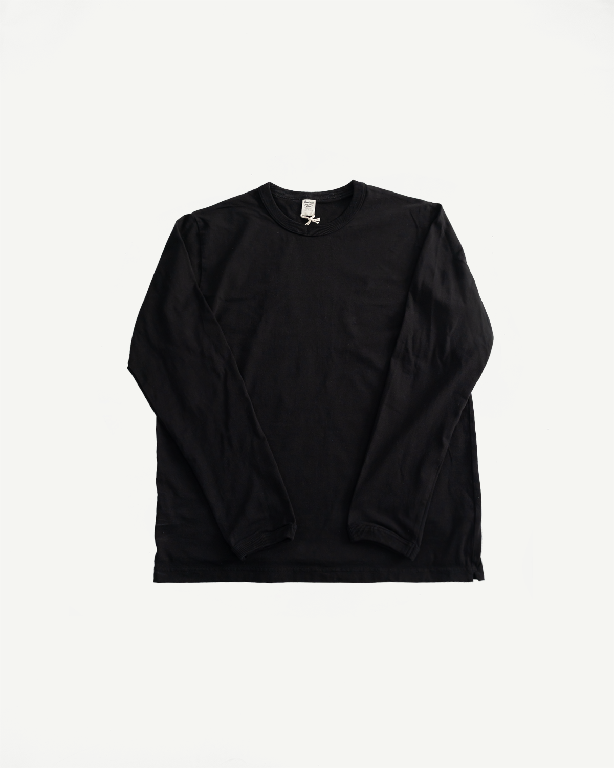 Flat lay front view of black long sleeve crewneck t-shirt, showing collar and tag details.