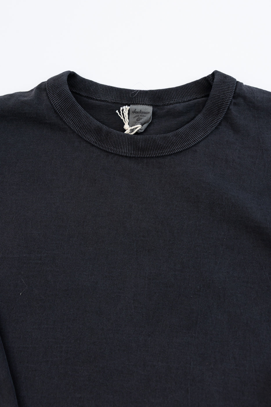 Close-up front view of black long sleeve tee, ribbed crew neck, Jackman tag visible, soft cotton texture