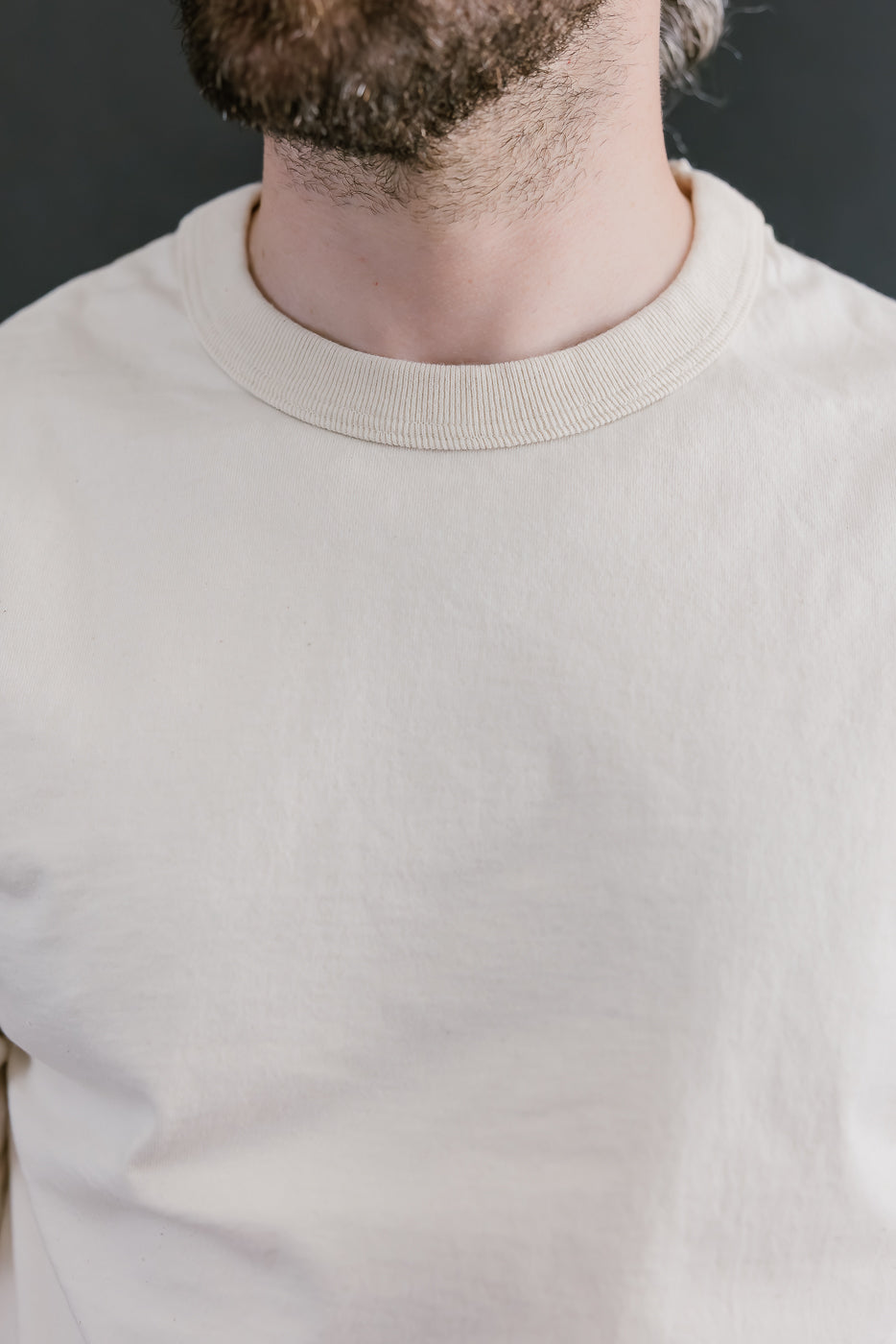 Close-up of a person wearing a beige sweater against a dark background