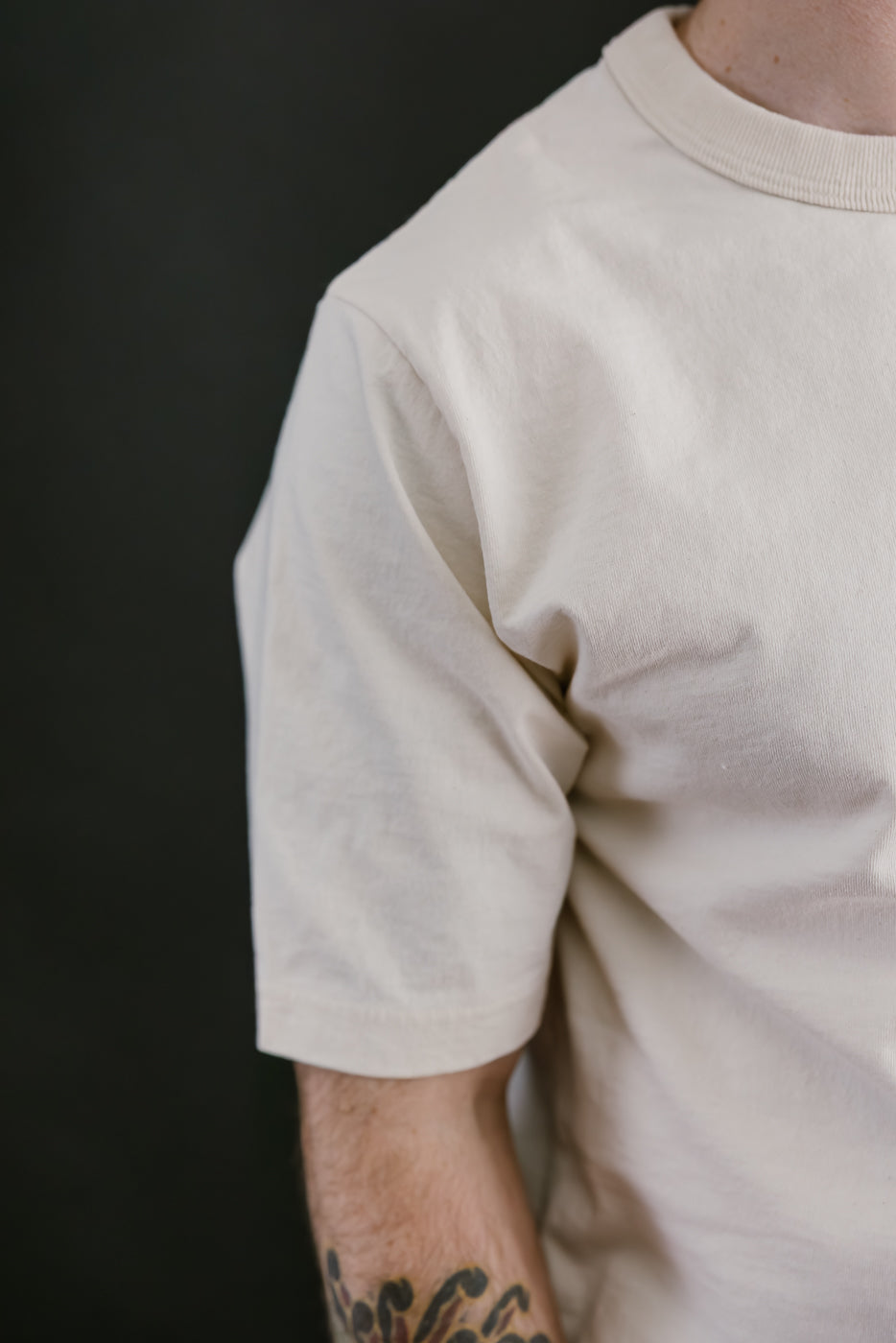 Person wearing a plain beige t-shirt against a black background