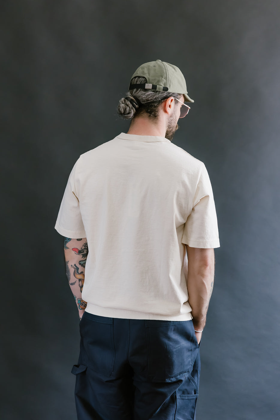 Man wearing a beige t-shirt and navy pants against a dark gray background