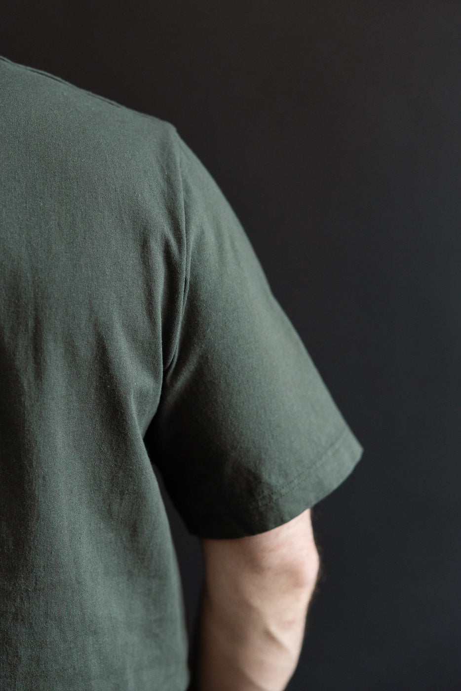 Close-up of male model's side, showing olive green T-shirt sleeve and fabric texture, athletic build