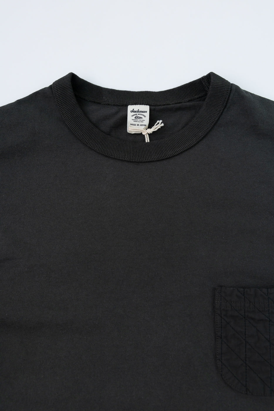 Close-up front view of black t-shirt with ribbed collar, tag, and quilted pocket detail