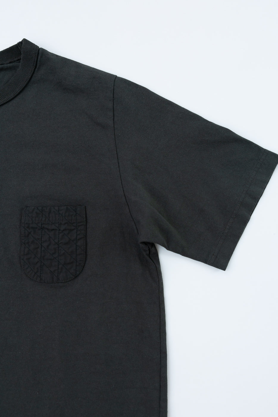 Black short-sleeve tee, front view close-up: ribbed crew neck, quilted chest pocket, clean hem