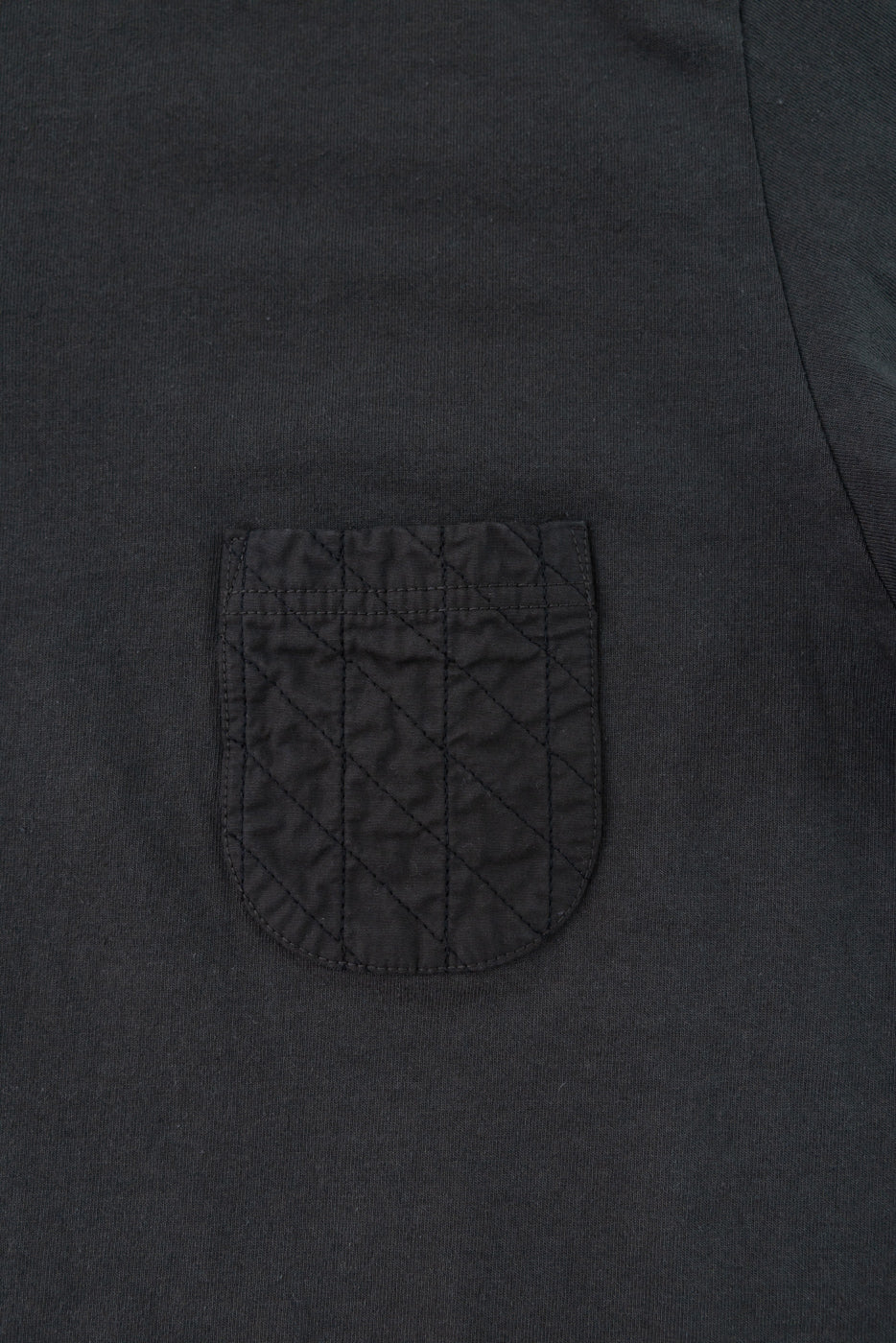 Close-up front view of dark charcoal t-shirt showing quilted chest pocket with diagonal stitching detail