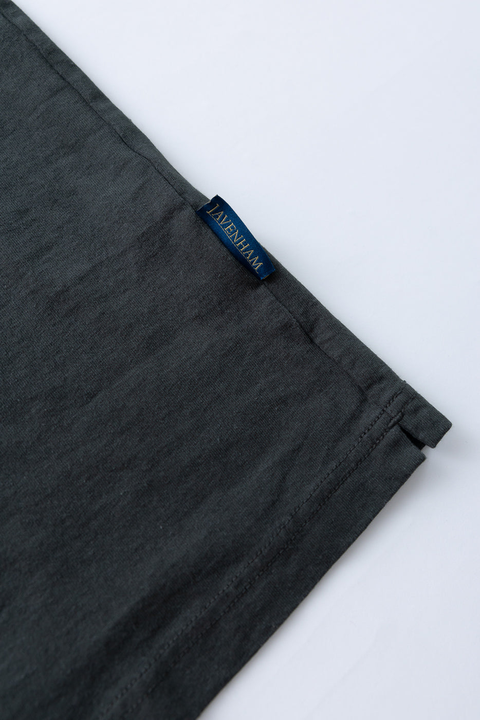 Close-up of dark gray garment hem with blue Lavenham tag, showing fabric texture and stitching detail