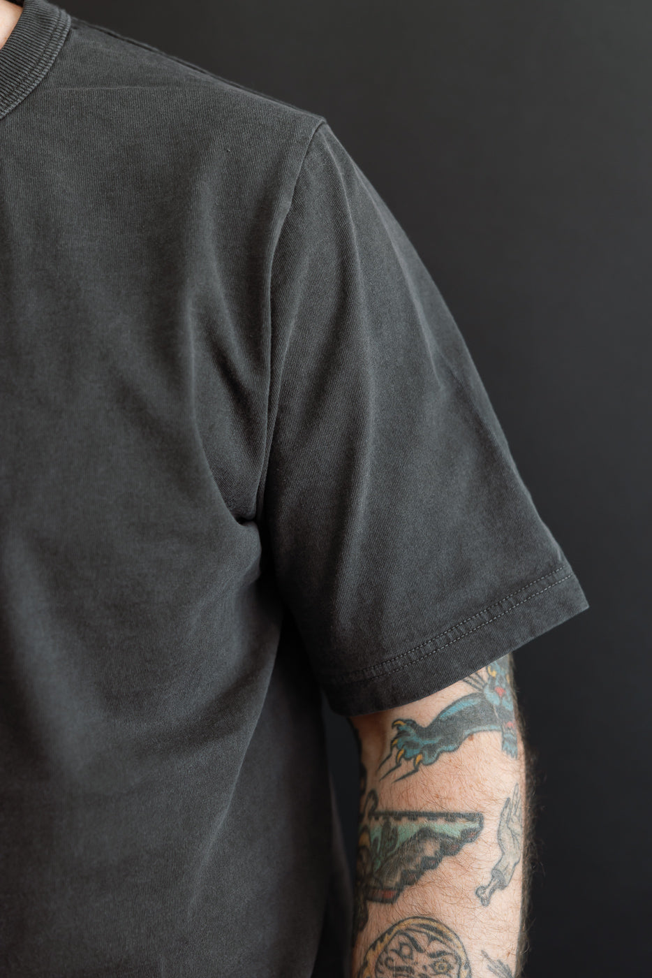 Close-up of male model's left side, showcasing dark gray t-shirt sleeve hem and ribbed collar detail.