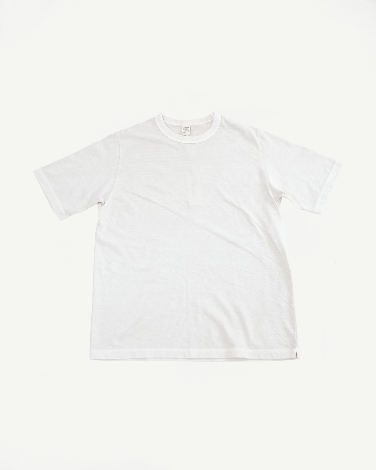 Front flat lay of white crew neck t-shirt, short sleeves, ribbed collar, tag visible, clean hem