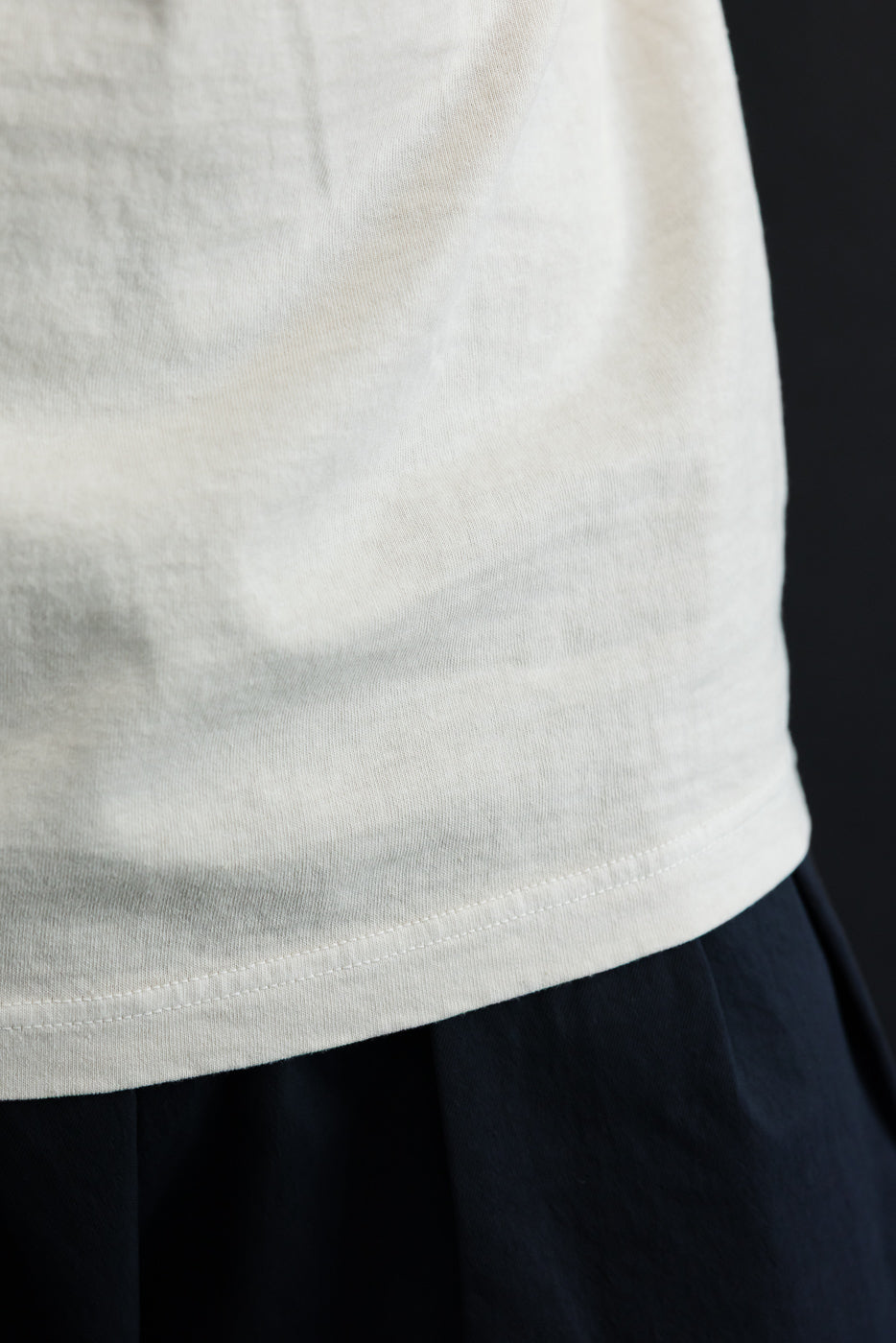Close-up of white t-shirt hem, showing clean stitching and soft fabric texture on male model.