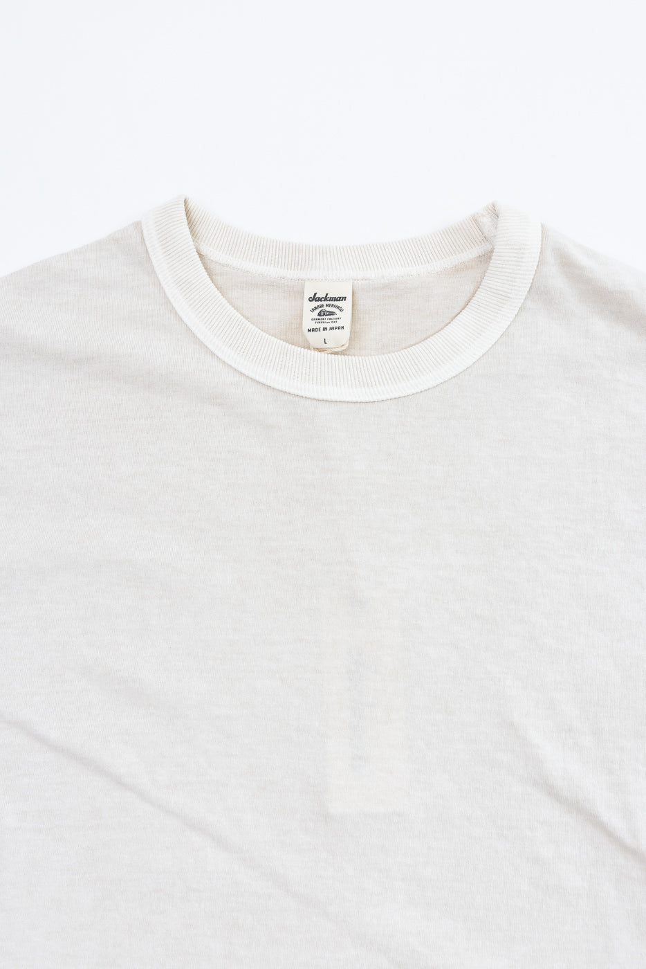 Close-up front view of cream crew neck tee, ribbed collar, Jackman tag, Made in Japan, soft cotton texture