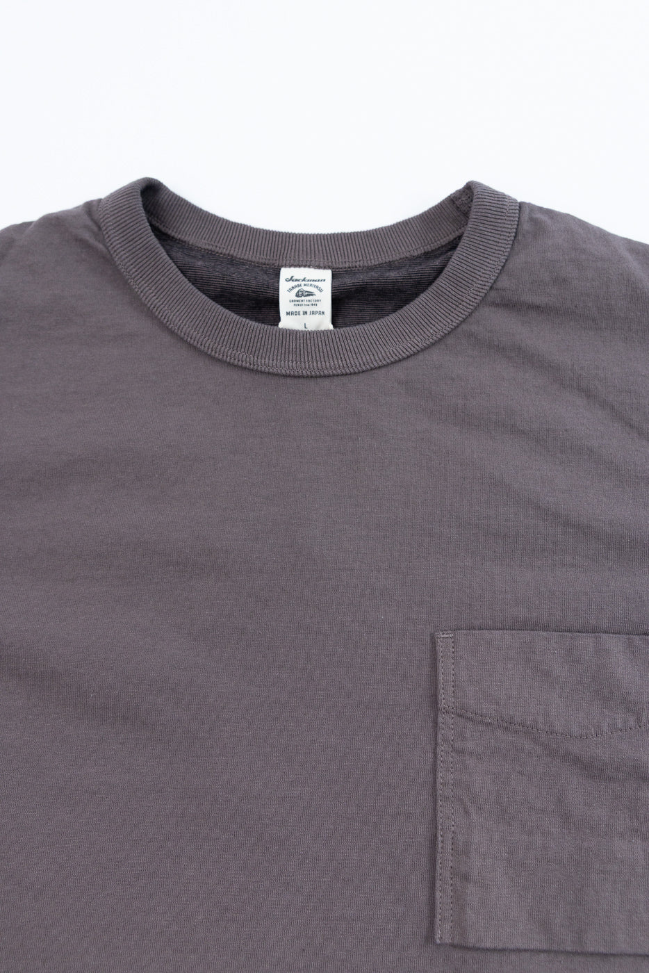 Close-up front view of gray crewneck tee with chest pocket, ribbed collar, and tag detail