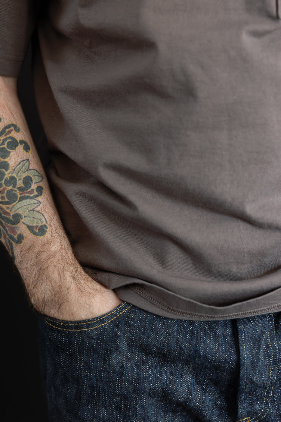 Close-up of male model's side, showing dark tee hem and selvedge denim texture, athletic build