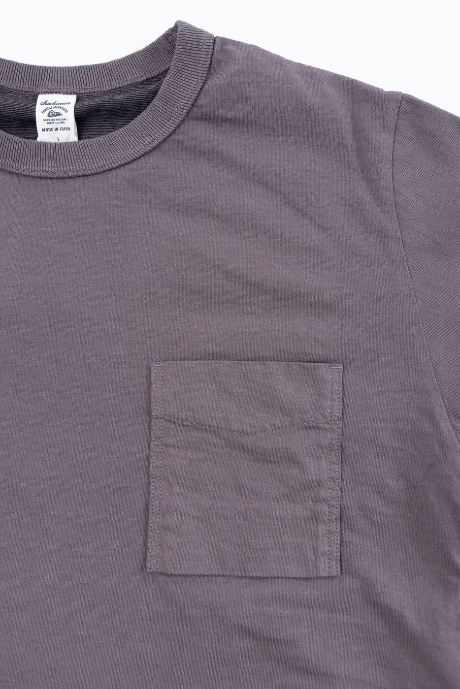 Close-up front view of gray t-shirt with chest pocket, ribbed collar, and tag detail