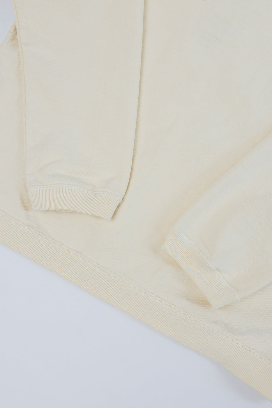 Close-up of the front bottom hem and ribbed sleeve cuffs of a cream sweatshirt.