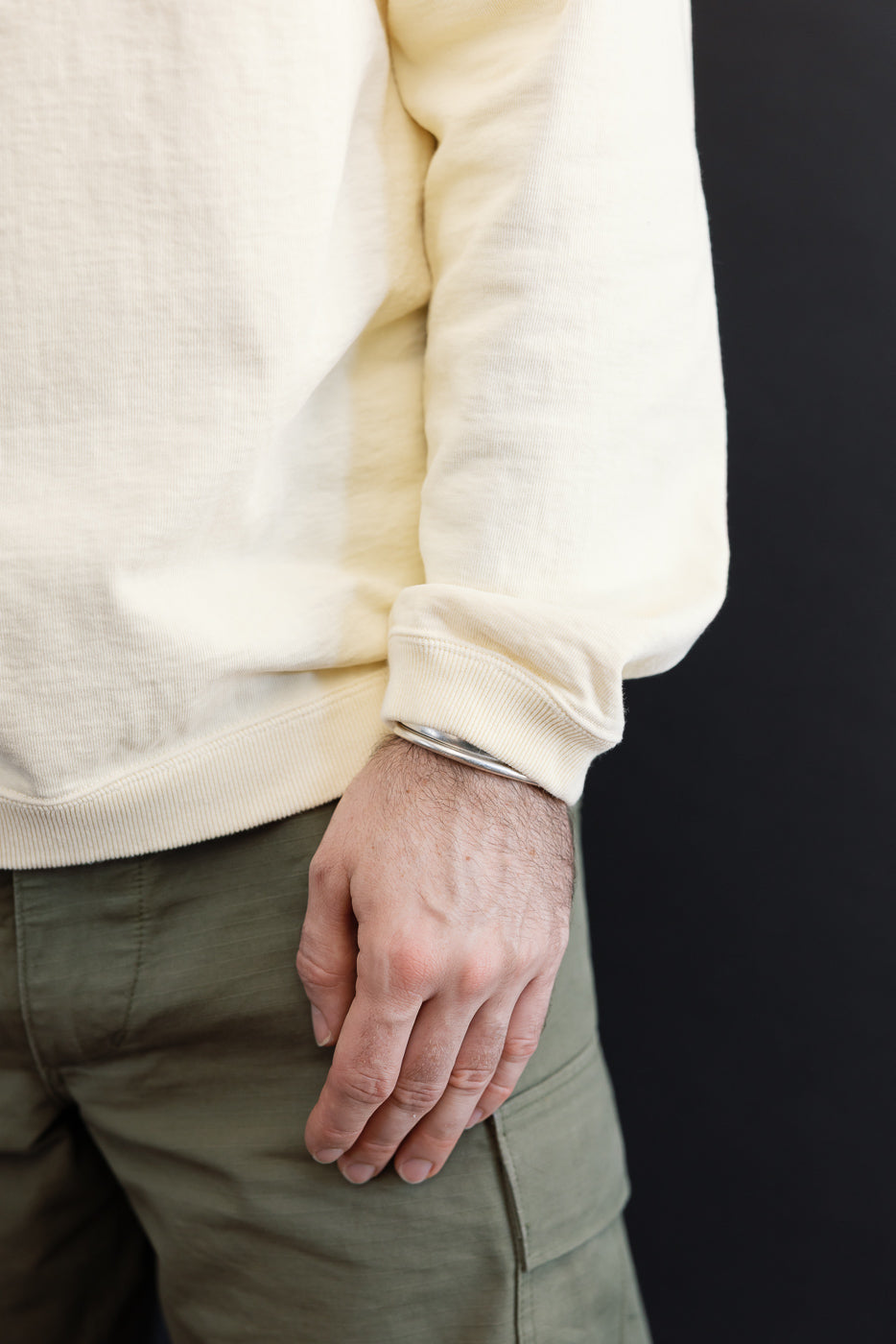 Close-up of the side and cuff of a cream sweatshirt and olive cargo pants on a male model.