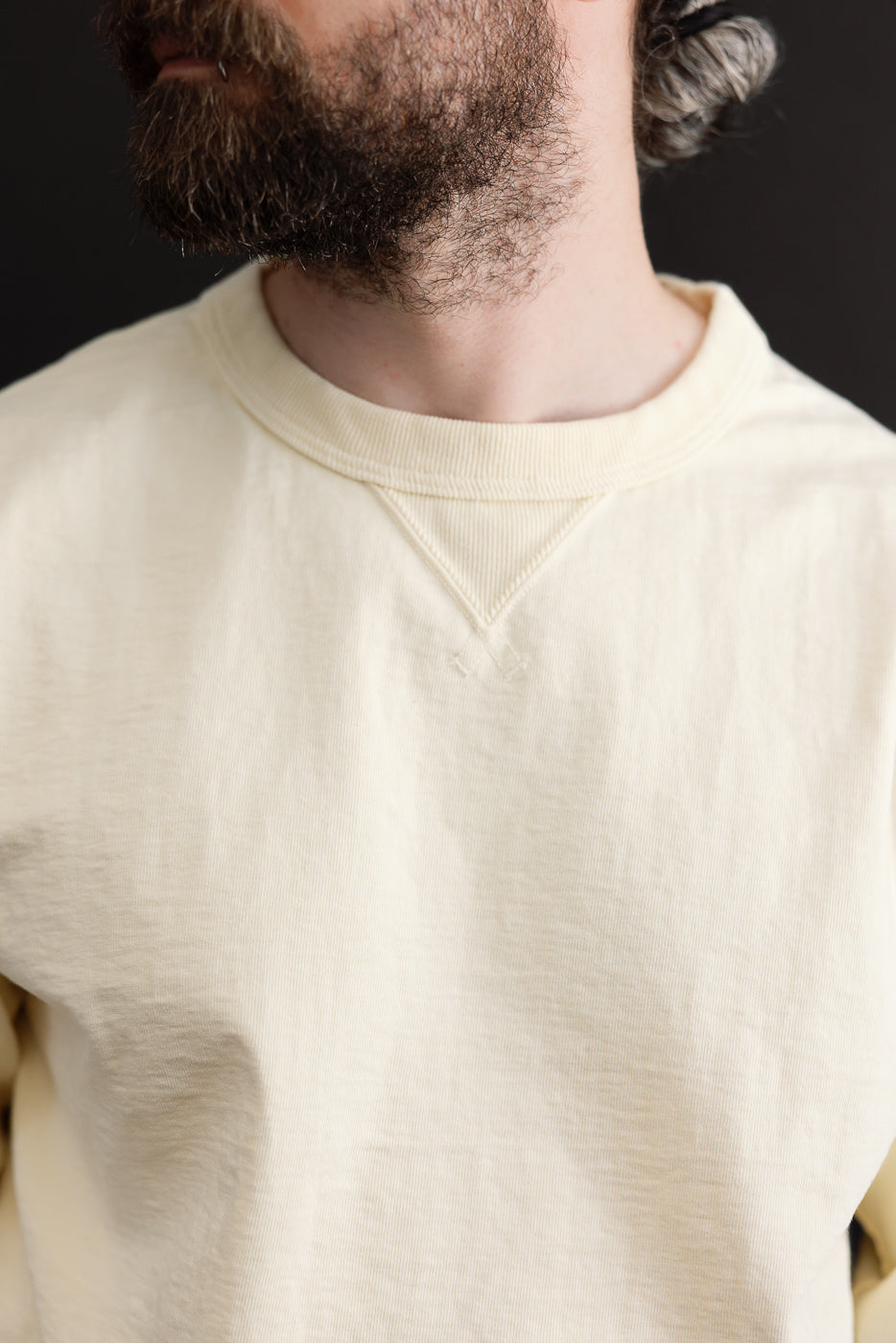 Close-up front view of the ribbed crewneck collar and fabric texture on a cream sweatshirt.