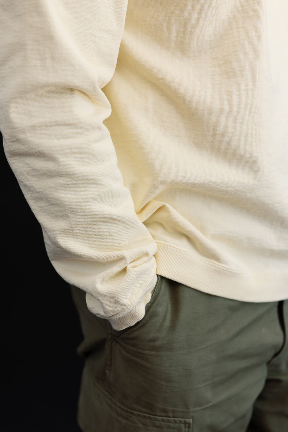 Close-up side view of a cream long-sleeve sweatshirt and olive green pants on a male model.