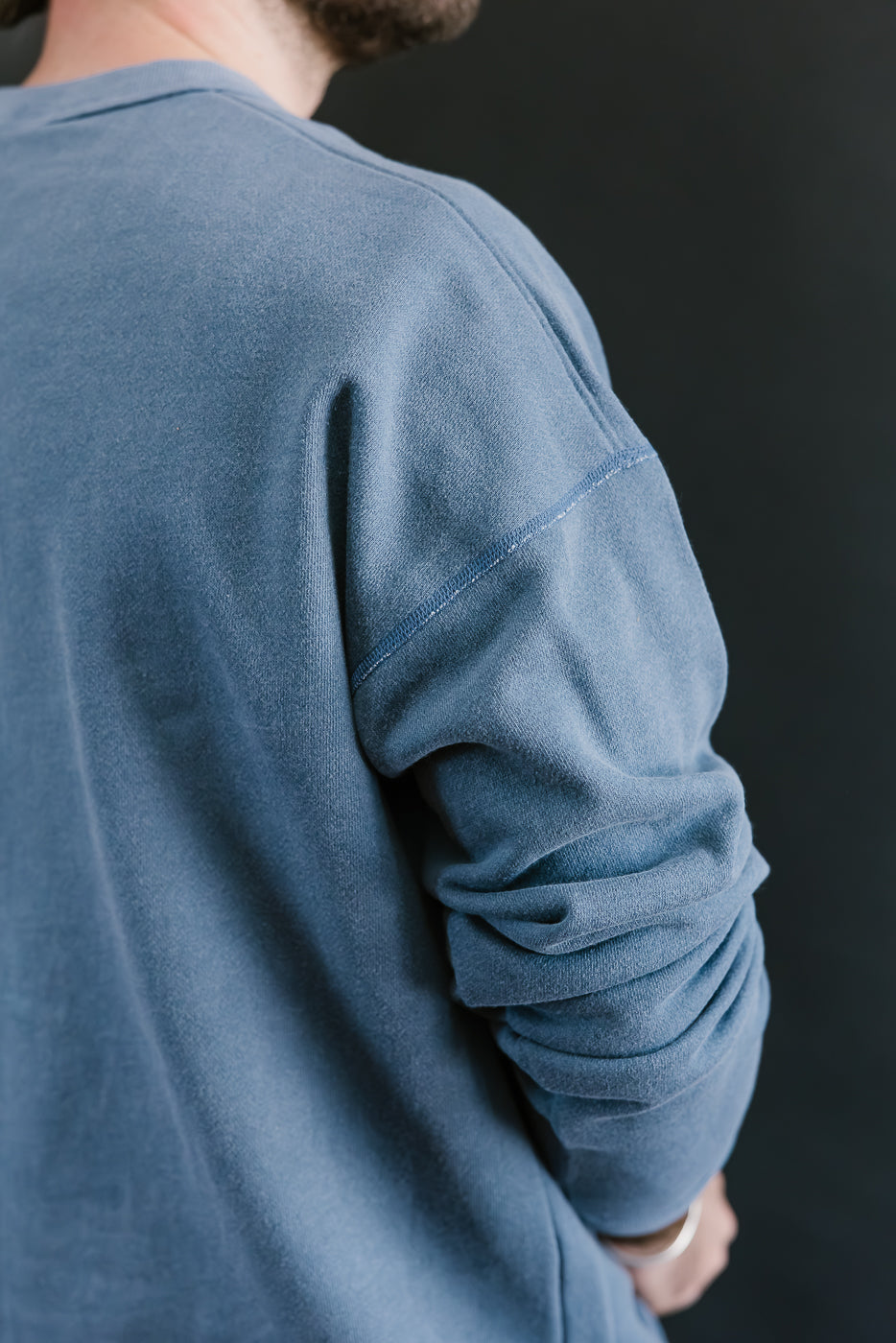 Person wearing a blue long-sleeve shirt against a dark background