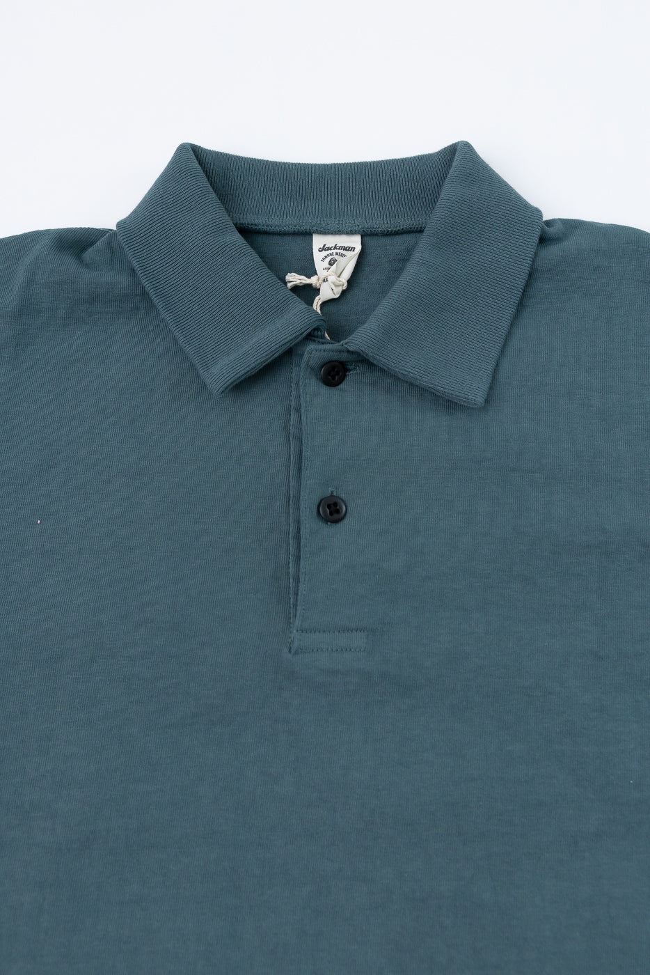 Close-up front view of teal polo shirt showing ribbed collar, black buttons, and Jackman brand tag on male model.