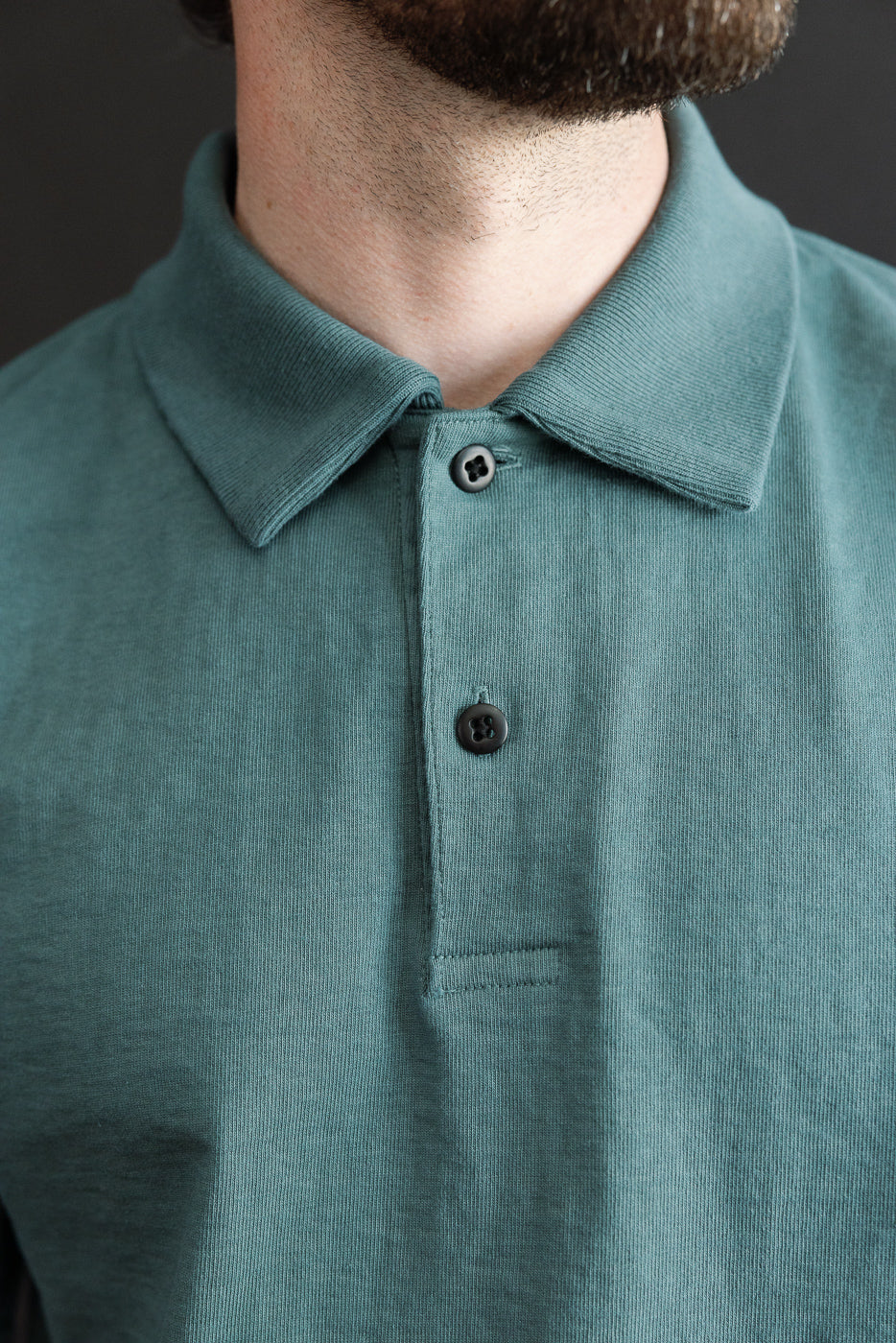Close-up front view of male model wearing teal polo shirt, showcasing collar, buttons, and fabric texture.