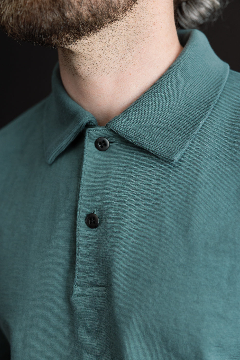 Close-up front view of male model wearing teal polo with ribbed collar and black buttons