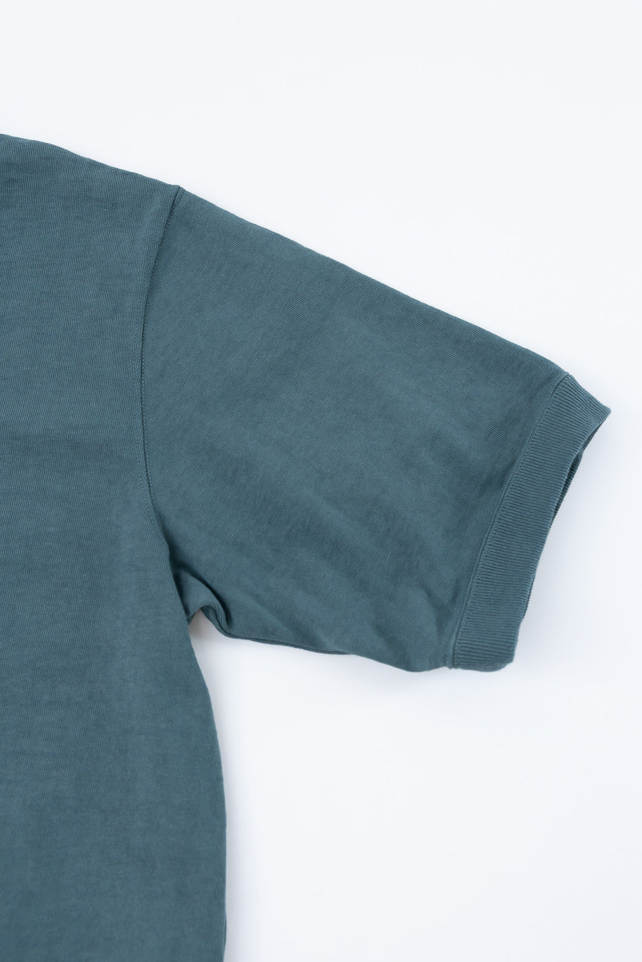 Close-up of teal t-shirt sleeve, ribbed hem, and shoulder seam detail