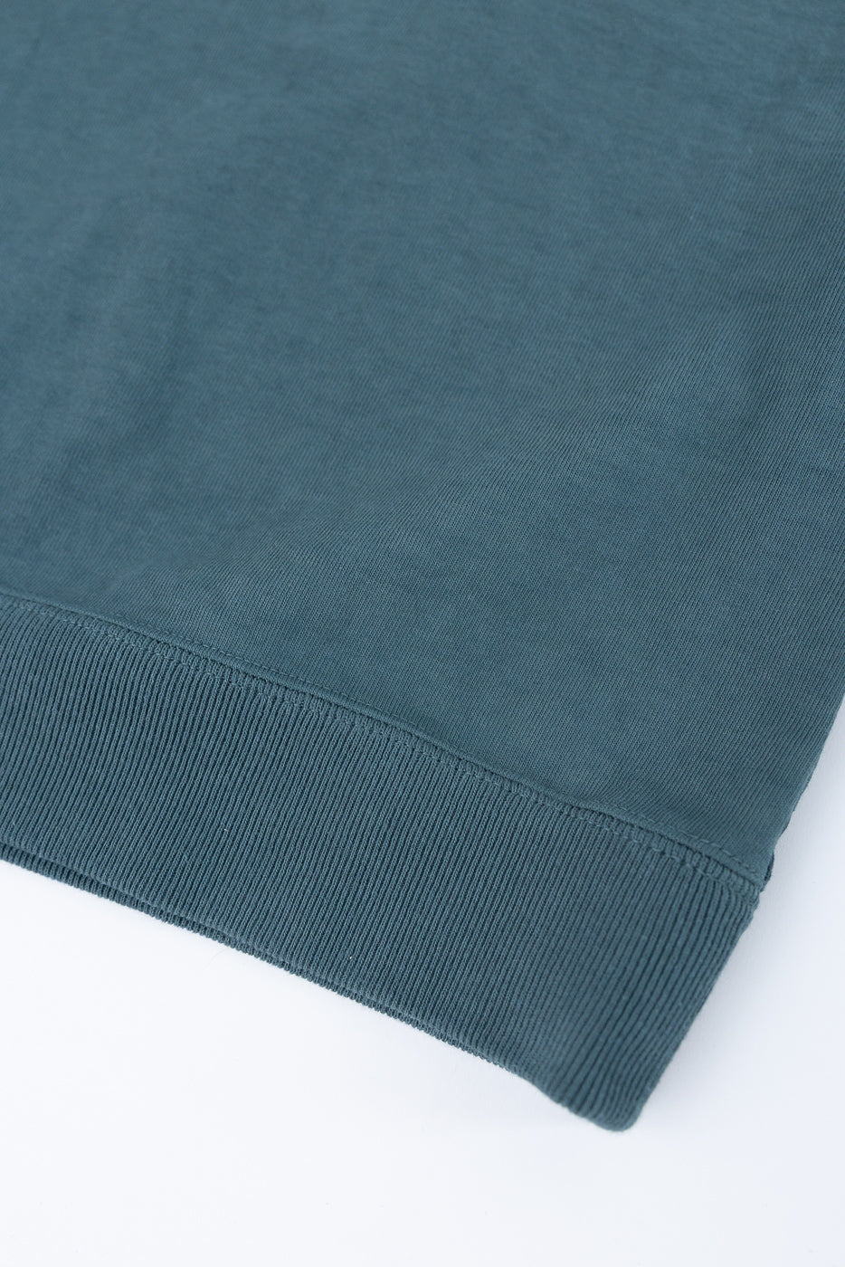 Close-up of teal crewneck sweatshirt hem, showing ribbed knit texture and clean stitching detail