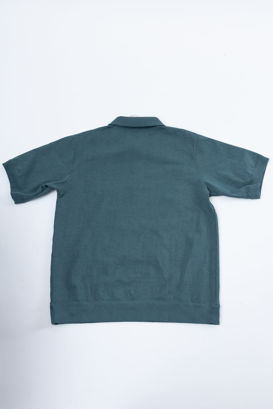 Back view of dark teal short-sleeve polo shirt with ribbed collar, cuffs, and hem, flat lay