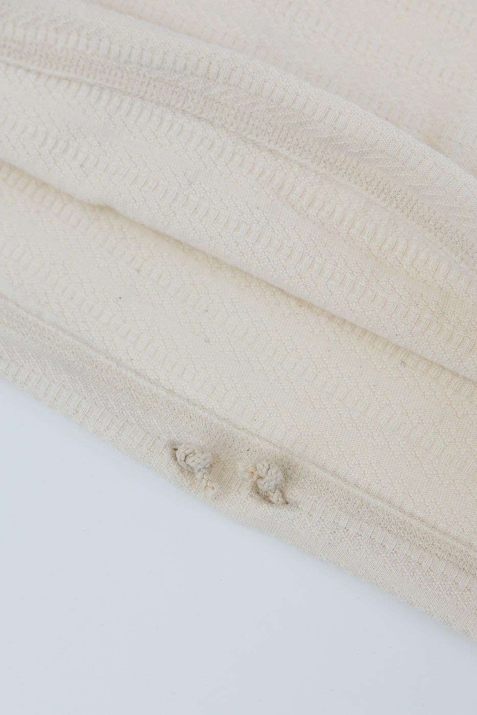 Close-up of ecru long sleeve t-shirt hem, showing knit texture and raw edge details, front view.