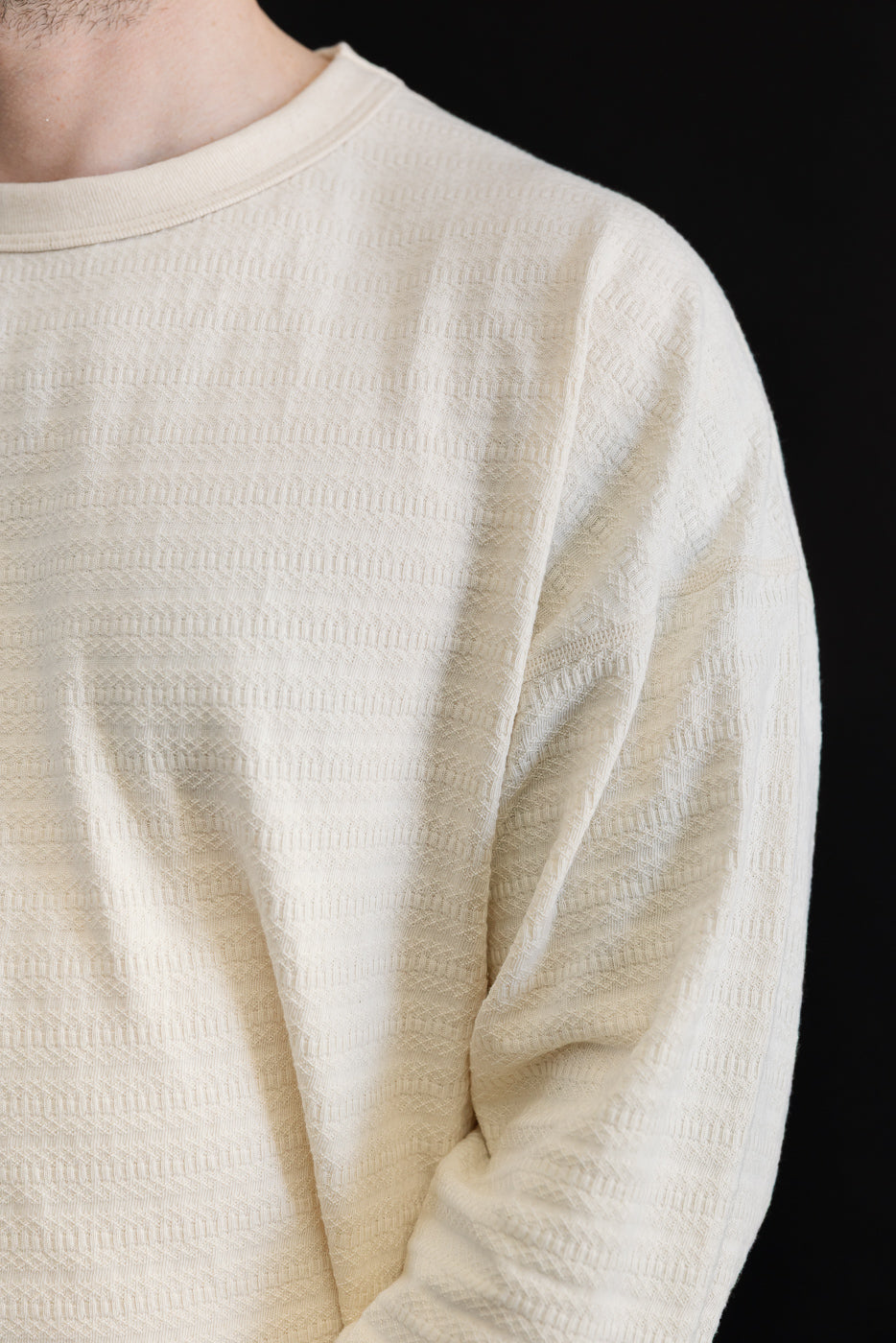 Close-up front of cream textured long sleeve t-shirt on male model, showing fabric detail.