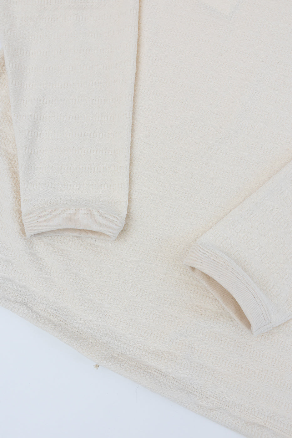 Close-up of ecru long sleeve t-shirt flat lay, showing front fabric texture and sleeve cuffs.