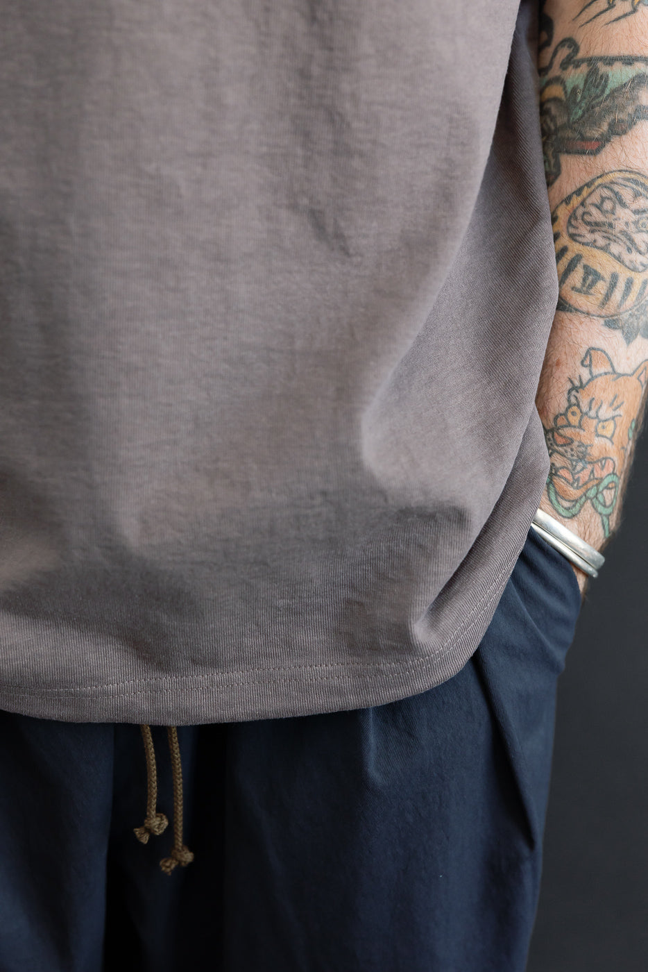 Close-up of gray t-shirt hem and navy drawstring shorts, worn by male model with tattooed arm