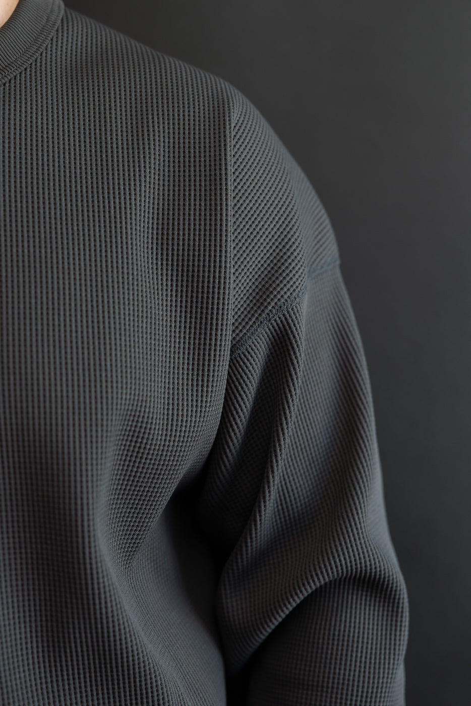 Close-up of male model's shoulder and sleeve, showcasing dark gray waffle-knit thermal texture and ribbed collar detail