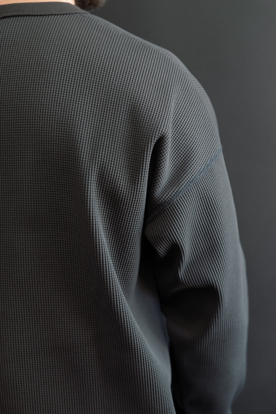 Close-up of male model's back, showcasing textured waffle knit shirt with shoulder seam detail