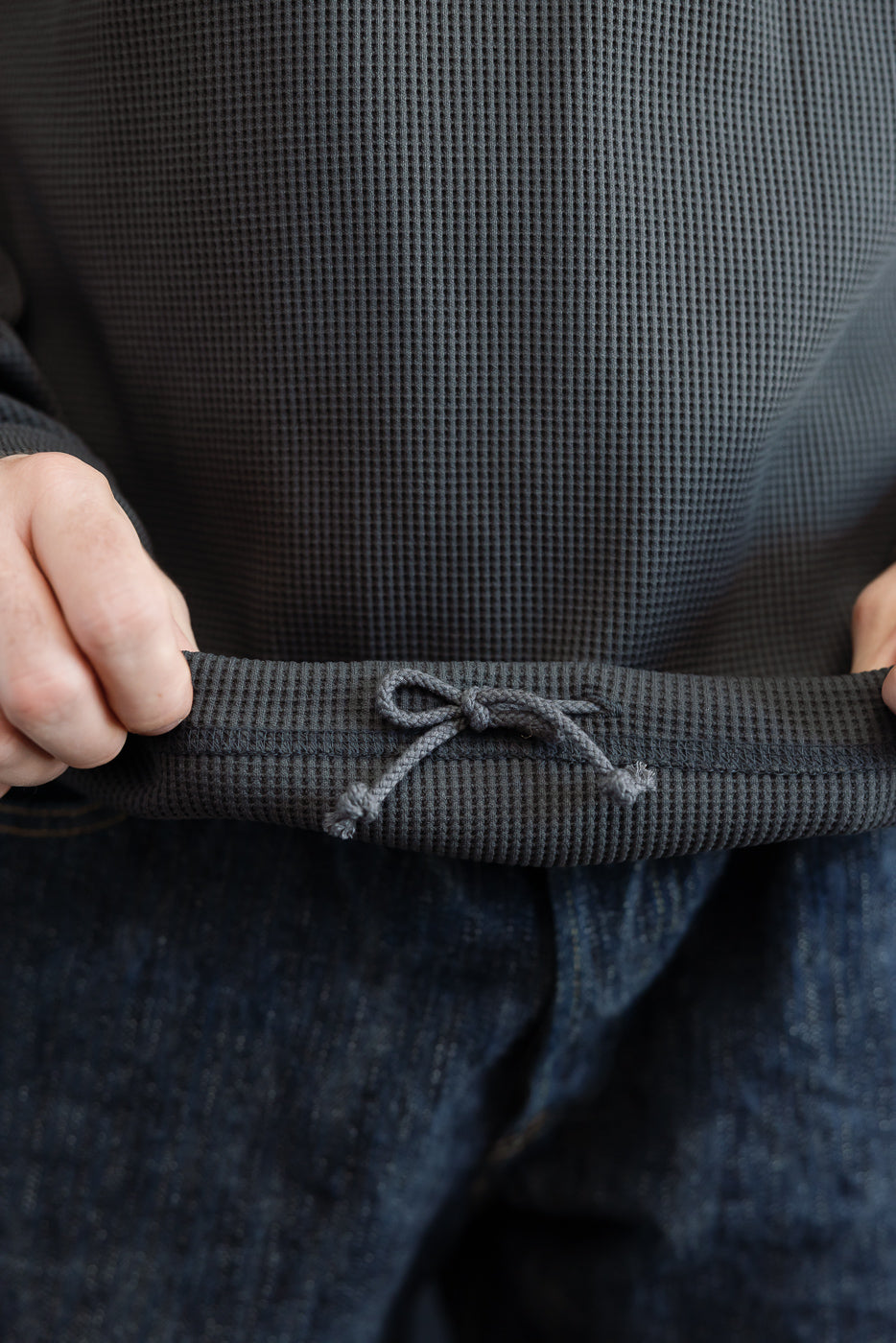 Close-up front view of male model's waist showing waffle knit sweatshirt with drawstring hem, athletic build
