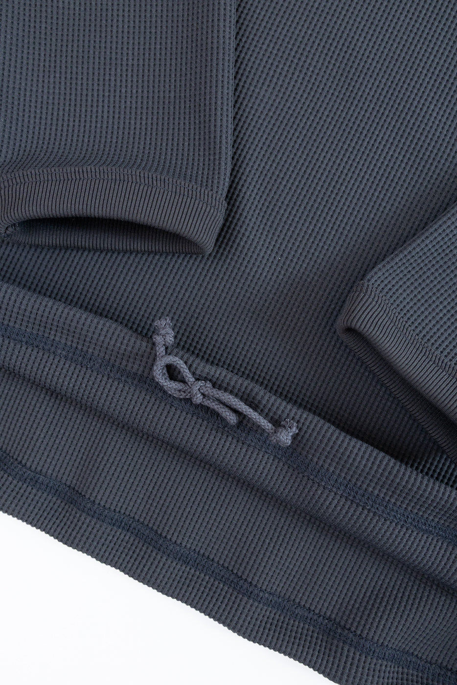 Close-up of dark gray waffle knit long sleeve hem with drawstring detail, front view